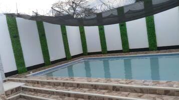 Una piscina con escalones de acceso, rodeada de muros blancos con detalles verticales verdes.