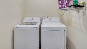 A laundry area with two white front-loading washing machines and a purple laundry basket on a shelf above. - Lake Hartwell Home Base: 2 Mi to Marina! (Hartwell)