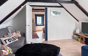 A cozy attic room with a sloped ceiling, a sofa with colorful pillows, a black throw blanket, a small white table, and a television on a wooden stand. - Awesome home in Fur with house sea view (Fur)