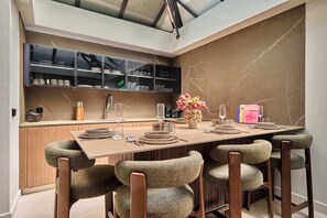 A modern dining area with a long table, six chairs, and a kitchen area with cabinets and a countertop. - Sublim Apartment - Le Marais - Beaubourg (Paris)