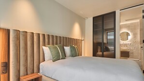 Une chambre moderne avec un grand lit, une table de chevet en bois et une porte-fenêtre coulissante donnant sur une salle de bain.