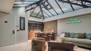 Un intérieur moderne doté d’un plafond en verre, d’un espace cuisine et d’un salon avec un canapé et des fauteuils.