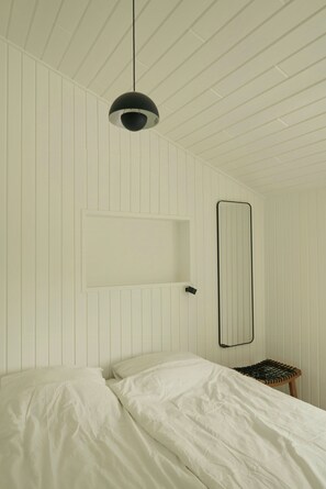 Ein Schlafzimmer mit einem Bett, einer Pendelleuchte, einem Spiegel und einem Hocker.