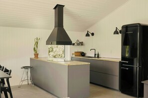 Uma cozinha moderna com uma ilha central, um exaustor preto, uma geladeira preta e uma janela com vista para o verde.