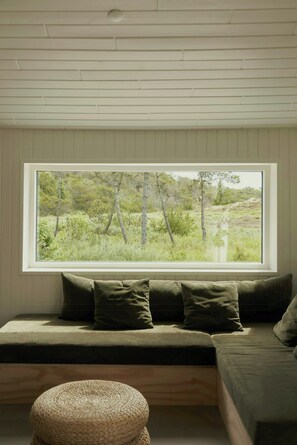 Ein Zimmer mit einem großen Fenster, einem grünen Sofa und einem gewebten Hocker.
