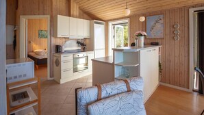 A compact kitchen with white cabinets, a stove, and a dining area with a table and chairs. - Beach front home in Vestervig with WiFi (Vestervig)