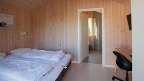A room with wooden walls, a bed with white bedding, a desk with a chair, and a door leading to another room. - Beach front home in Vestervig with WiFi (Vestervig)