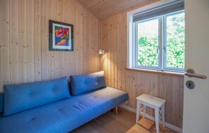 Ein Zimmer mit einem blauen Sofa, einem kleinen weißen Tisch, einem gerahmten abstrakten Gemälde und einem Fenster mit Blick auf Grünflächen.