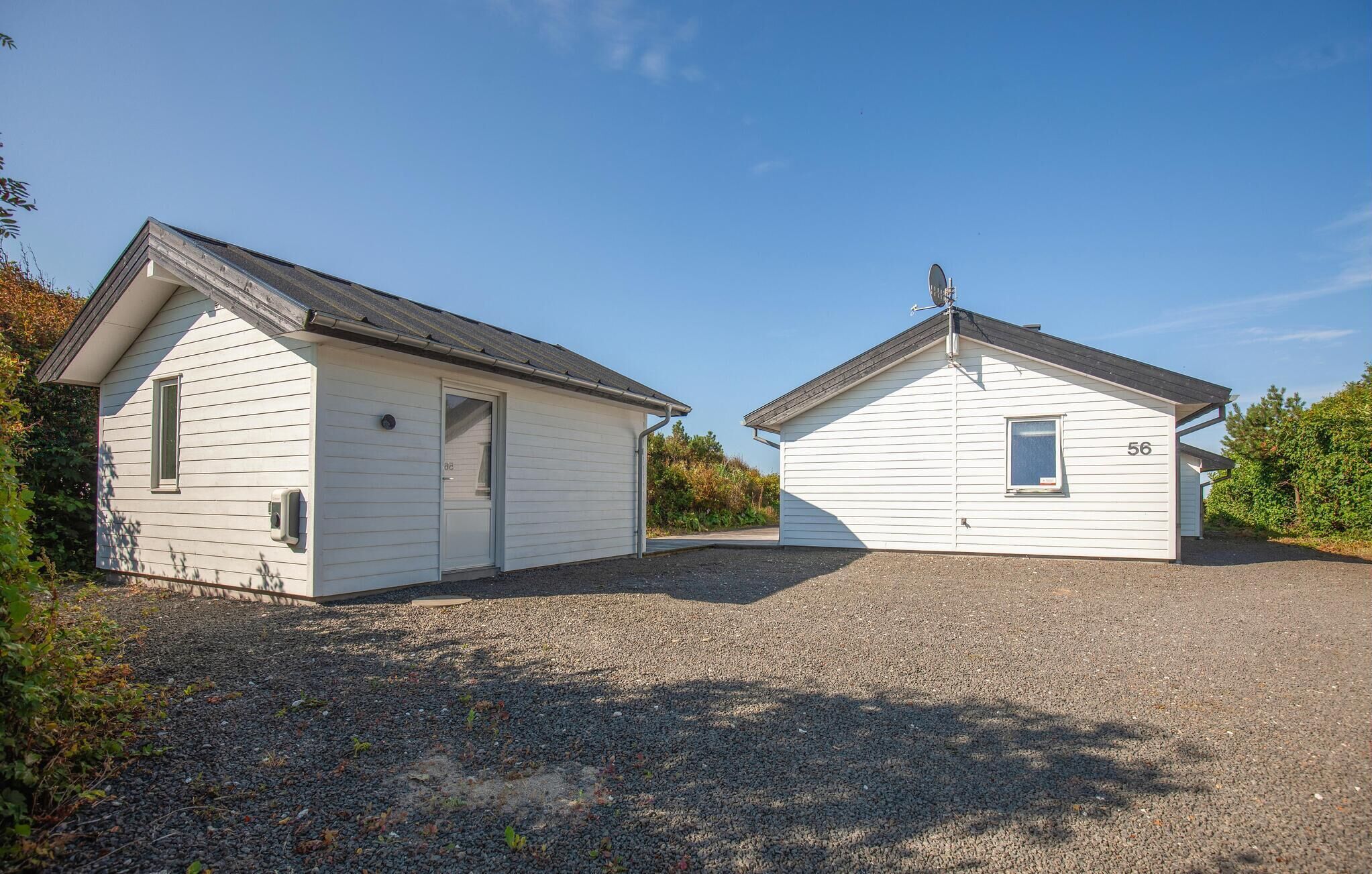 Two small, single-story buildings with sloped roofs, a gravel driveway, and a clear blue sky.