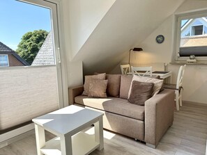 A modern loft bedroom with a sloped ceiling, a sofa, a small table, and a view of the outside. - Reiherweg, Apartment 3 - Beautiful 2-room vacation apartment with a south-facing balcony, quiet and (Sylt)