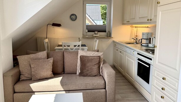 Ein gemütliches Schlafzimmer im Loft-Stil mit schrägverdeckter Decke, einer Couch mit Kissen, einem Nachttisch und einem Fenster mit Blick auf ein Haus.