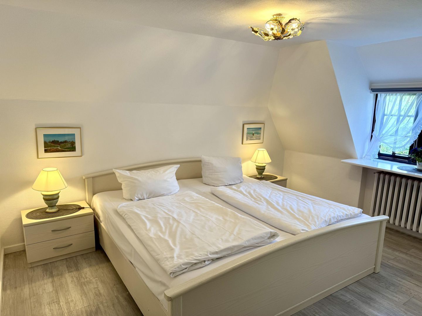 A bedroom with a bed, two bedside tables, two lamps, a window, and a radiator.