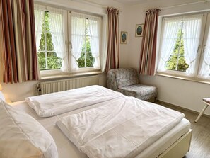 A bedroom with two beds, a chair, and windows with curtains. - Süderstraße, Apartment 05 – Landhaus - Cozy 2-room vacation apartment for 4 (Sylt)