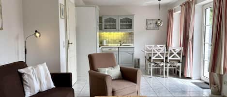 Una sala de estar moderna con un sofá marrón, una mesa de centro de madera con revistas y un comedor con sillas blancas.