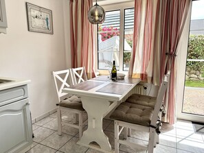A dining area with a white table and chairs, a bottle of wine, and a framed picture on the wall. - Süderstraße, Apartment 05 – Landhaus - Cozy 2-room vacation apartment for 4 (Sylt)