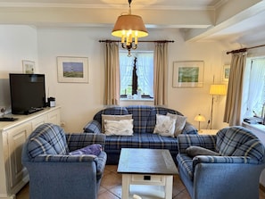 Ein Wohnzimmer mit einer Sofagarnitur, einem Fernseher und einer Lampe.