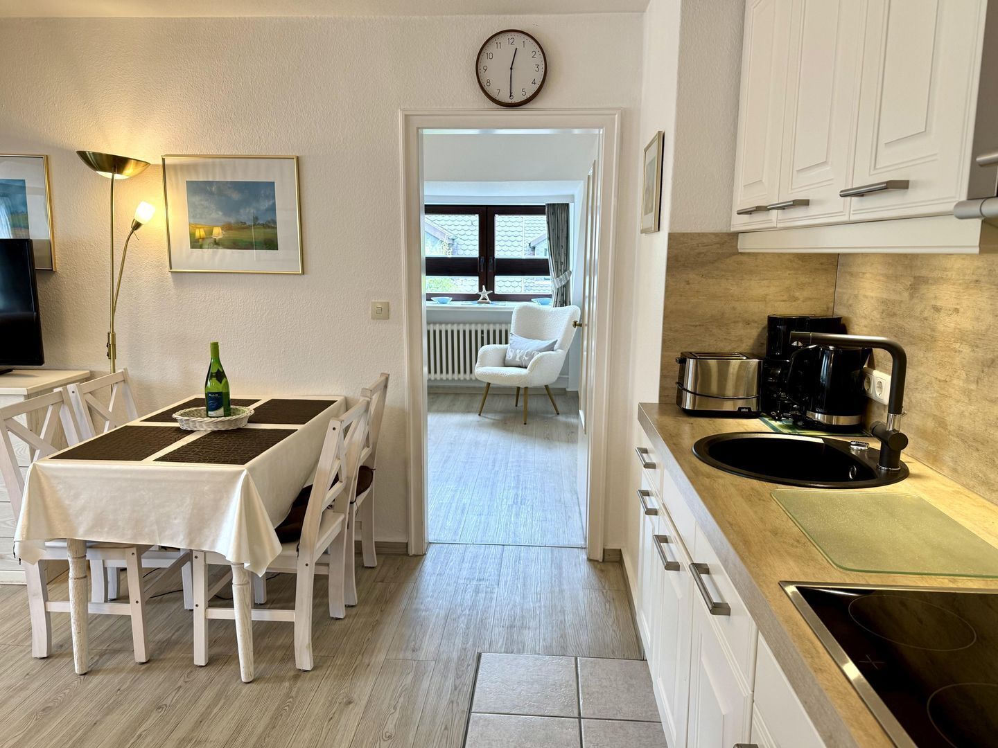 A modern kitchen with white cabinets, a black stove, and a dining area with a table and chairs.