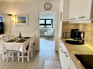 A modern kitchen with white cabinets, a black stove, and a dining area with a table and chairs. - Puan-Stöven-Weg, Apartment 2 - Cozy 2-room vacation apartment for 2 people, (Sylt)