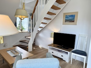Ein modernes Wohnzimmer mit Treppe, Flachbildfernseher und Essbereich.