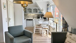 Et moderne køkken med hvide skabe og et spiseområde med et bord og stole. En sofa med pude og en lampe er i forgrunden.