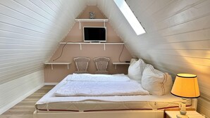 Et soveværelse med skrå væg, en seng, et sengebord med lampe og et fjernsyn på en hylde.