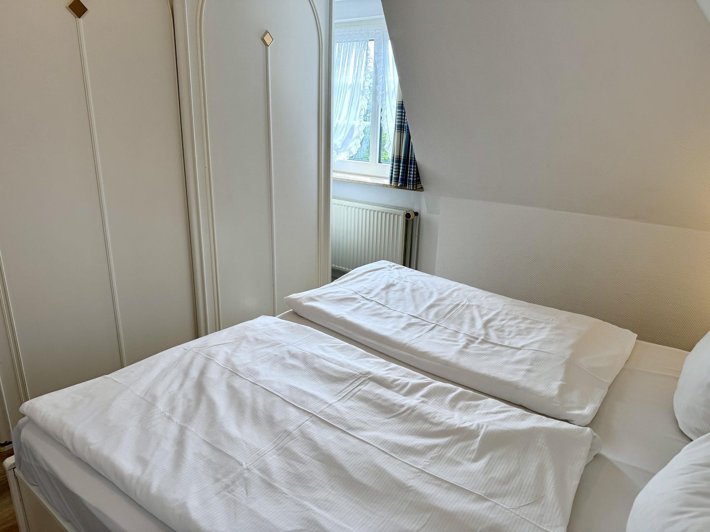 Een slaapkamer met een bed, een raam met gordijnen en een radiator.