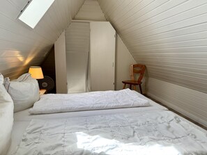 A small, single-bed room with a sloped ceiling, a wooden chair, and a bedside table with a lamp. - Süderstraße, Apartment 11 – Landhaus - Cozy 3-room vacation apartment for 4 (Sylt)