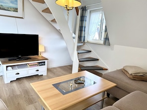A modern living room with a flat-screen TV, a coffee table, a sofa, and a staircase with a view. - Süderstraße, Apartment 08 – Landhaus - Cozy 3-room vacation rental for 4 (Sylt)