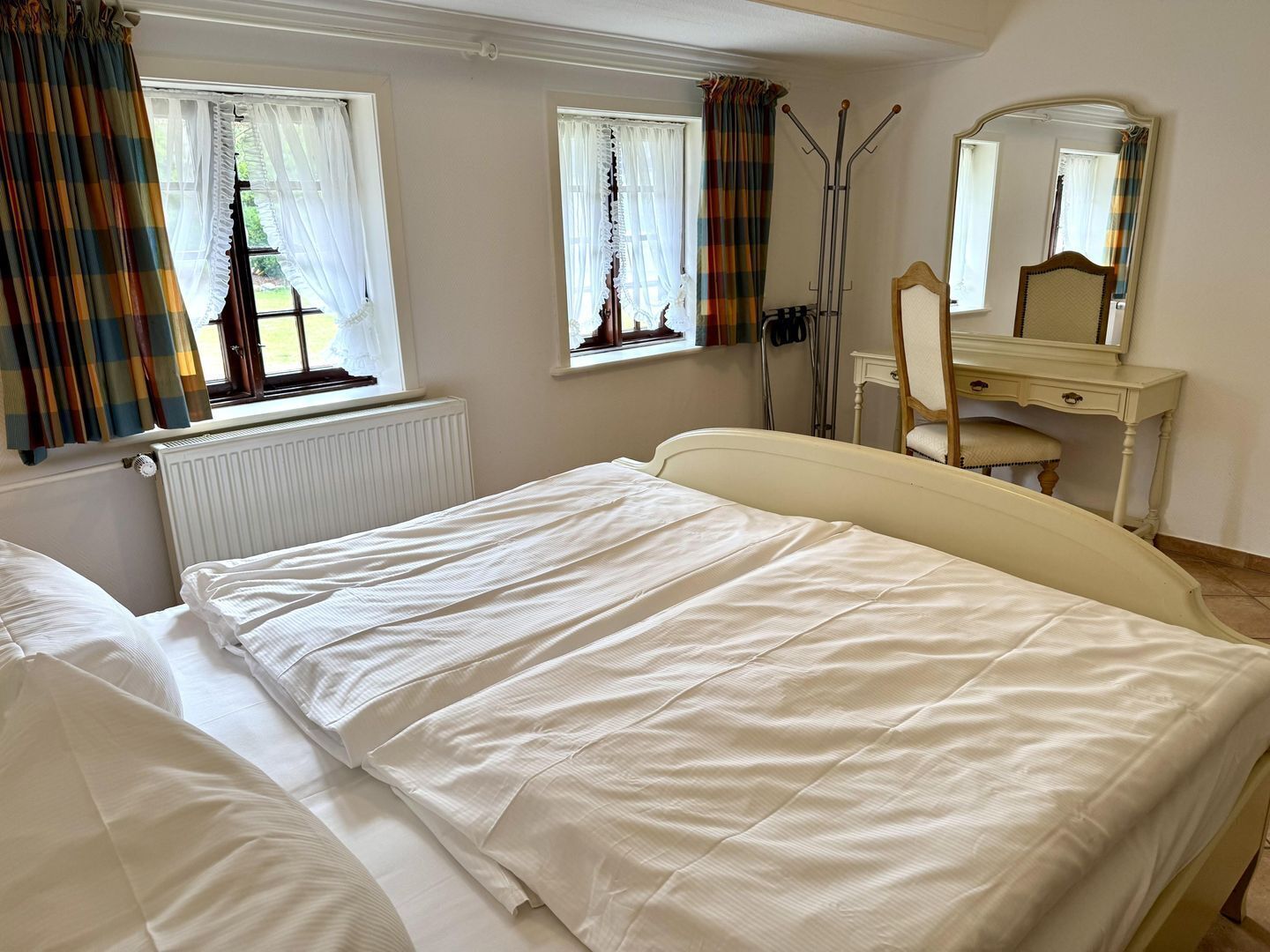 A bedroom with a bed, a dresser, a mirror, and windows with curtains.