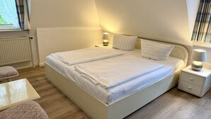 A double bed with two bedside tables, a chair, and a window with curtains. - Süderstraße, Apartment 07 – Landhaus - Cozy 3-room vacation rental for 4 (Sylt)
