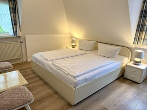 Ein Doppelbett mit zwei Nachttischen, einem Sessel und einem Fenster mit Vorhängen.