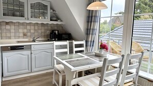 A kitchen with a dining area, featuring a white table and chairs, a coffee maker, and a view of the outside. - Süderstraße, Apartment 07 – Landhaus - Cozy 3-room vacation rental for 4 (Sylt)