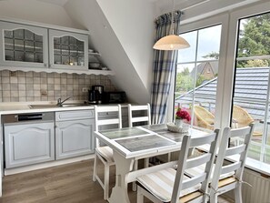 Eine Küche mit Essbereich, ausgestattet mit einem weißen Tisch und Stühlen, einer Kaffeemaschine und Blick ins Freie.