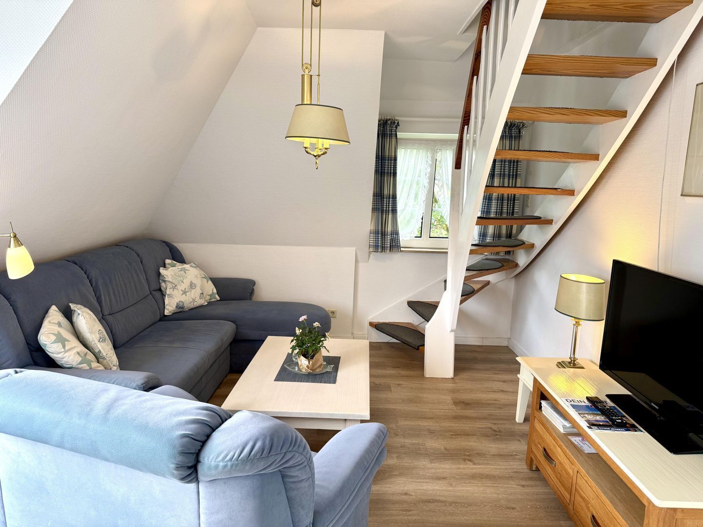 A modern loft-style living space with a sofa, coffee table, TV, and a staircase.
