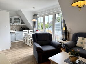 Eine moderne Küche mit weißen Schränken, einem Esstisch und Stühlen. Ein schwarzes Ledersofa und ein kleiner Tisch mit Blumenvase sind ebenfalls vorhanden.