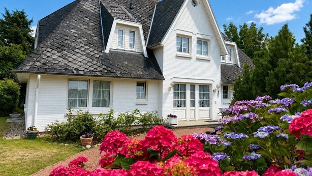 A two-story house with a steeply pitched roof, white siding, and a front porch with a bench. - Süderstraße, Apartment 07 – Landhaus - Cozy 3-room vacation rental for 4 (Sylt)