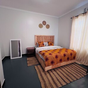 A bedroom with a wooden headboard, a bed with patterned bedding, a bedside table, a mirror, and a woven rug.