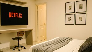 Una camera da letto con un letto, una scrivania con un computer, una sedia e una televisione che mostra il logo Netflix.