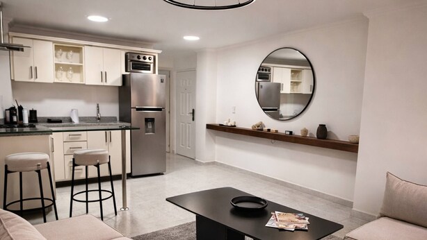 Una cucina moderna con elettrodomestici in acciaio inossidabile, uno sgabello da bar e uno specchio rotondo appeso al muro.