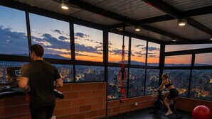 A gym with a treadmill, stationary bike, and exercise ball, with a city view through large windows. - Luxury Loft  Jacuzzi, Gym and steam bath  Laureles (Medellín)