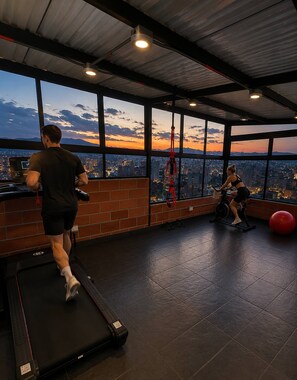 A gym with a treadmill, stationary bike, and exercise ball, with a city view through large windows. - Luxury Loft  Jacuzzi, Gym and steam bath  Laureles (Medellín)