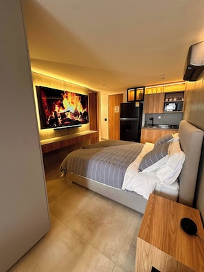 A modern bedroom with a large bed, a flat-screen TV mounted on the wall, a built-in kitchen area, and a wooden nightstand. - Luxury Loft  Jacuzzi, Gym and steam bath  Laureles (Medellín)