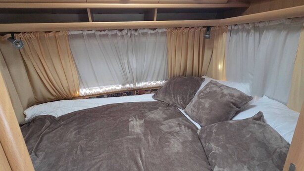 A bed with a headboard, curtains, and a window with a view.