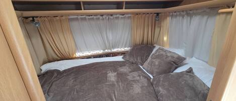 A bed with a headboard, curtains, and a window with a view.