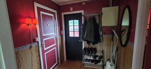 Un couloir doté d’un plancher en bois, d’une porte noire et d’un meuble à chaussures contenant plusieurs paires de chaussures.