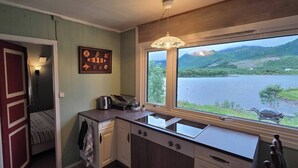 A kitchen with a view of a lake and mountains, a kettle, and a clock on the wall.
