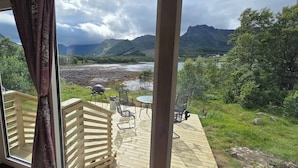 A wooden deck with outdoor seating and a view of a river and mountains.