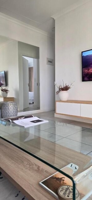 A modern living room with a glass coffee table, a sofa, and a television.