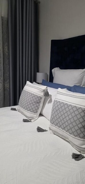 A hotel room with a neatly made bed, a dark headboard, and a lamp on the nightstand.