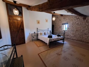 A bedroom with a stone wall, a bed with a metal frame, a wooden door, and a small window. - Starling Lodge rural holiday (Le Fleix)